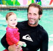 A man holding a baby in front of an indoor pool.